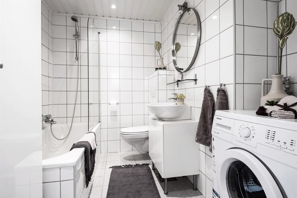 Lyst og tiltalende bad med hvit baderomsinnredning, innmurt badekar og opplegg for vaskemaskin. Galleribilde