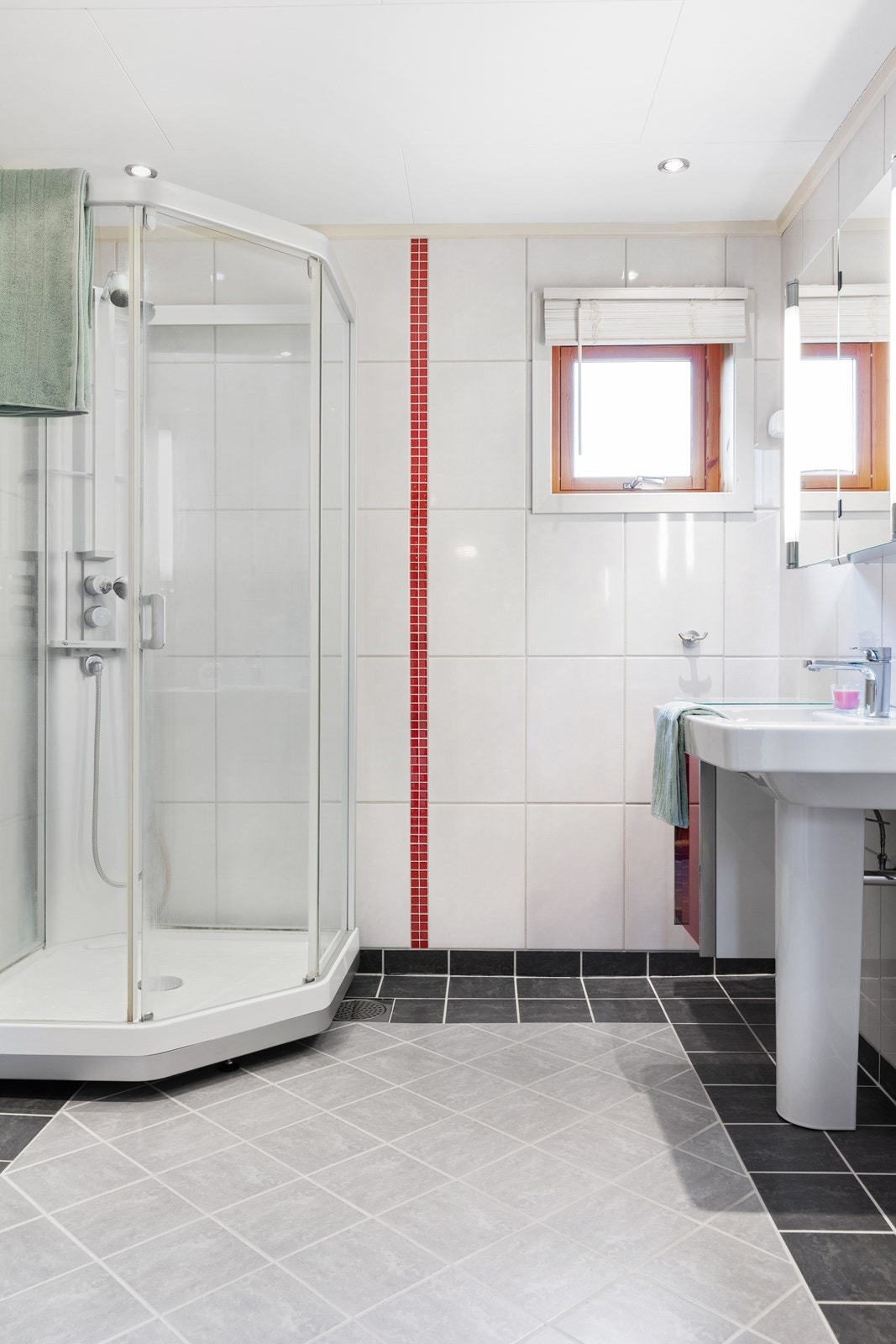 Badet har bl.a. flislagte gulv- og veggoverflater, varmekabler i gulv, integrert belysning i himling, dusjkabinett og vegghengt klosett. Galleribilde