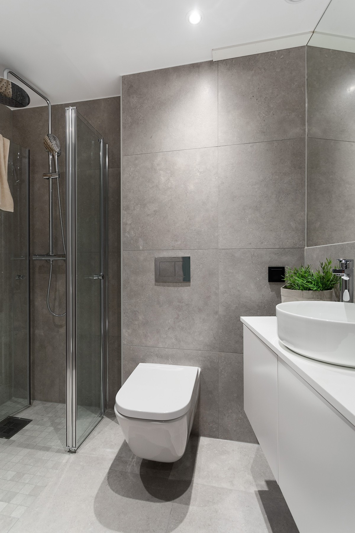 Lekkert bad med varmekabler, betongflis på gulv, mosaikk i dusjsonen, limt speil på hel vegg, dusj med svingbare dusjdører i glass, veggmontert wc, servant på benkeplate samt opplegg for vaskemaskin. Galleribilde