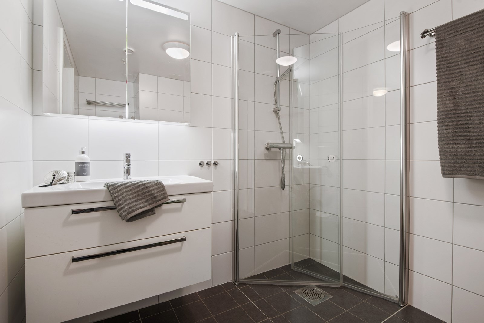 Badet er utstyrt med baderomsinnredning med lyse fronter, servant med speilskap og belysning, vegghengt toalett og opplegg for vaskemaskin. Romslig dusj med glassdører Galleribilde