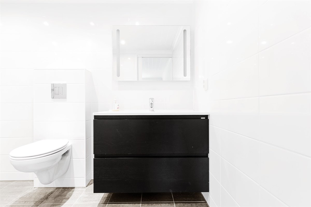 Vegghengt toalett og pen baderomsinnredning som bryter mot det ellers lyse badet. Galleribilde
