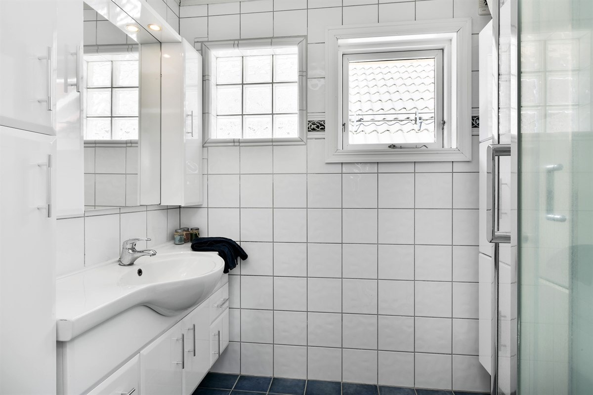 Badet er eldre og har hvite veggfliser kombinert med blå fliser på gulv med varme. Galleribilde