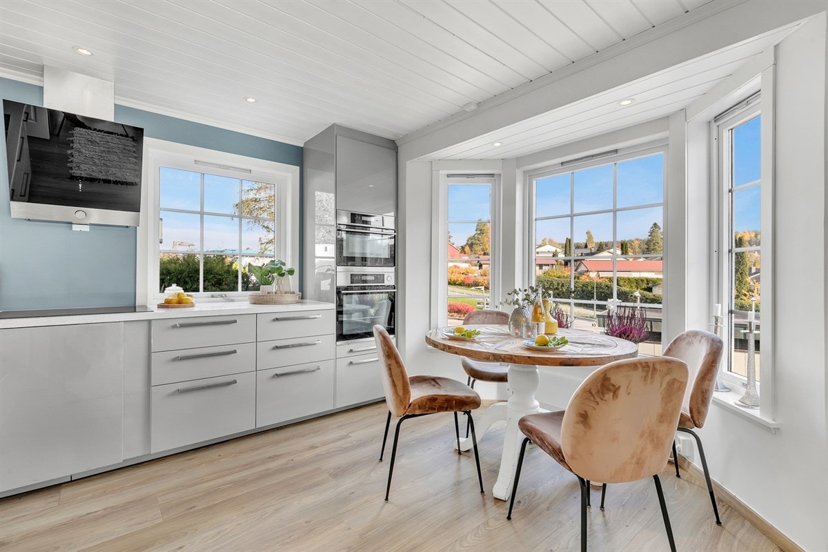 Kjøkkenet har laminat på gulv, enkelte downlights, vegger i delikat blåfarge og en hyggelig spiseplass ved et stort karnapp. Galleribilde