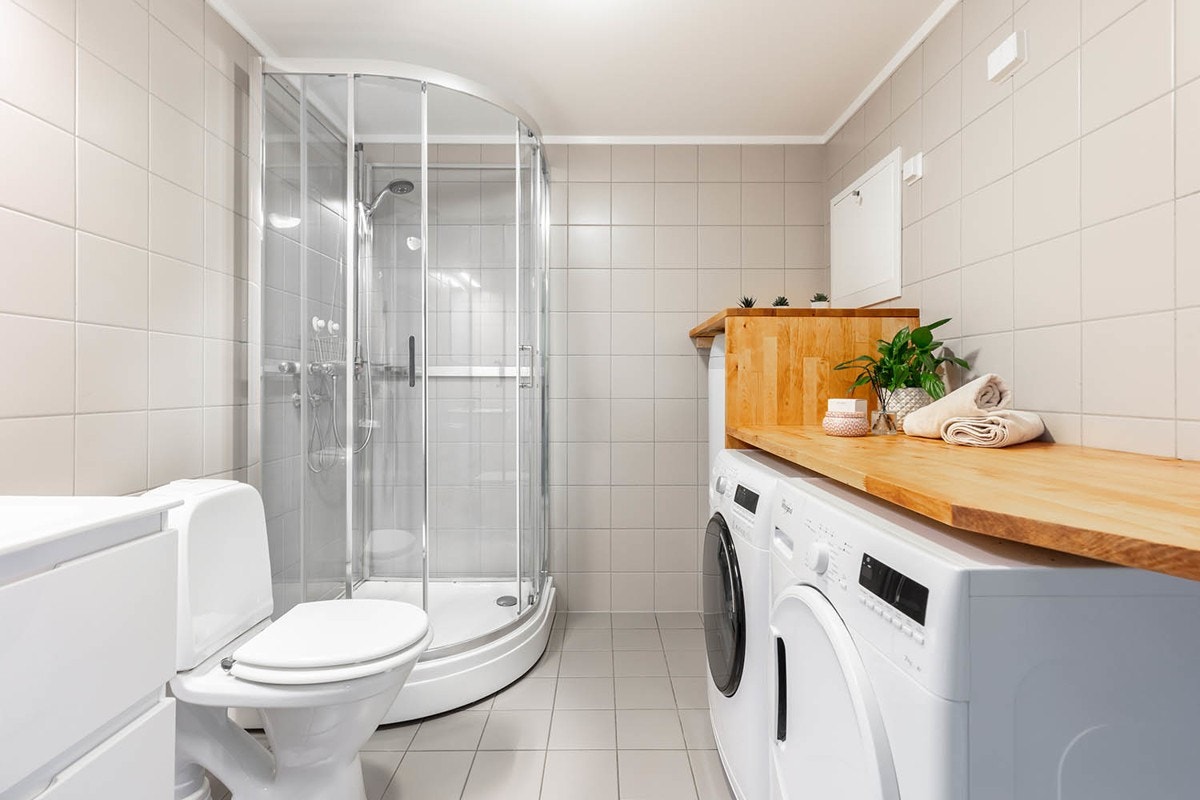 Badet inneholder dusjkabinett, toalett og en heldekkende servant med innredning med skuffeseksjoner med hvite glatte fronter. Galleribilde