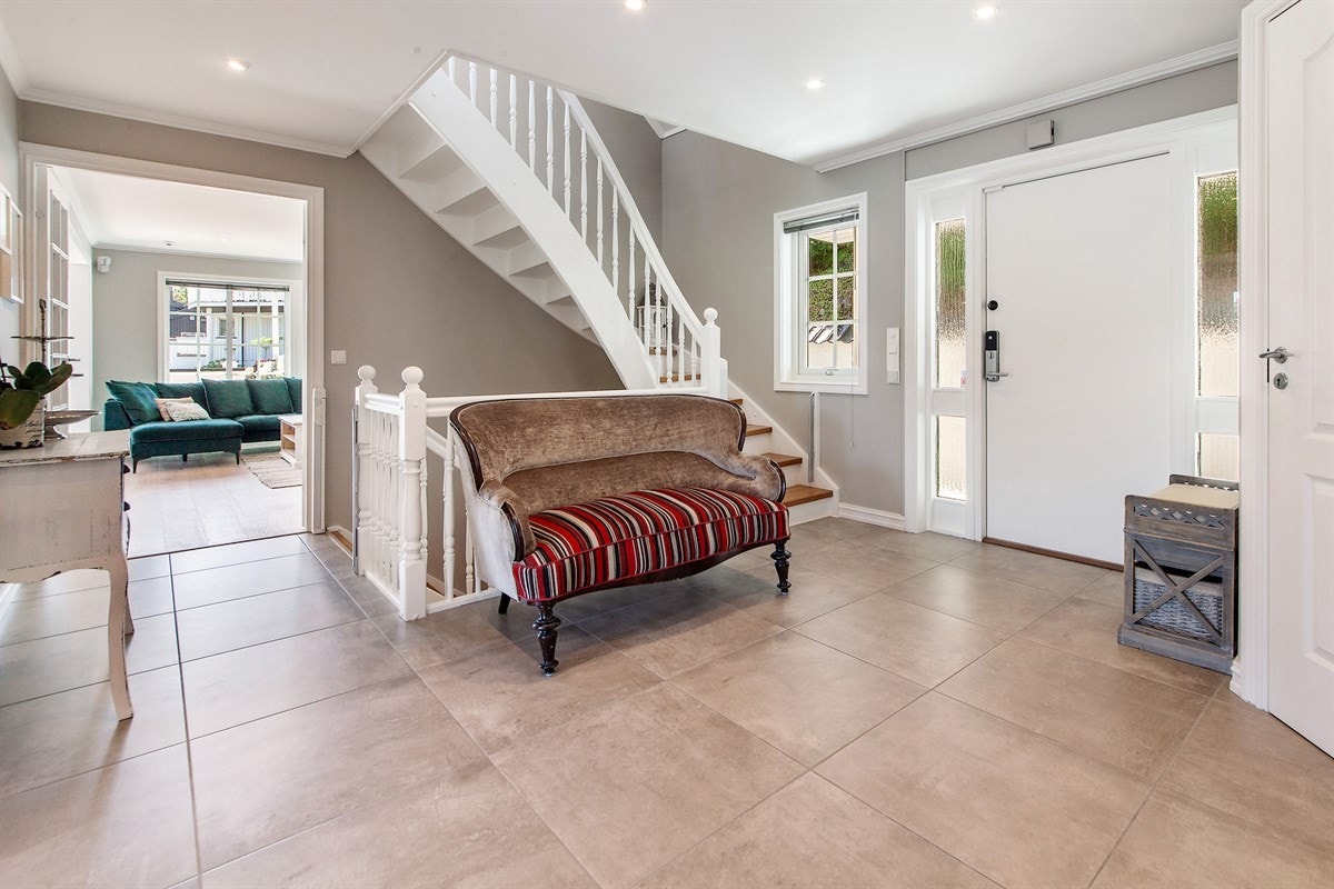 Hallen på innsiden er romslig og lys med grå vegger, store, sandfargede gulvfliser og downlights. Galleribilde