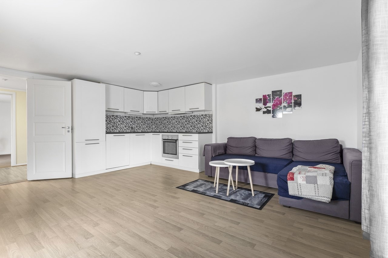 Boligen har en romslig åpen stue/kjøkkenløsning med parkett på gulv og lysmalte vegger Galleribilde