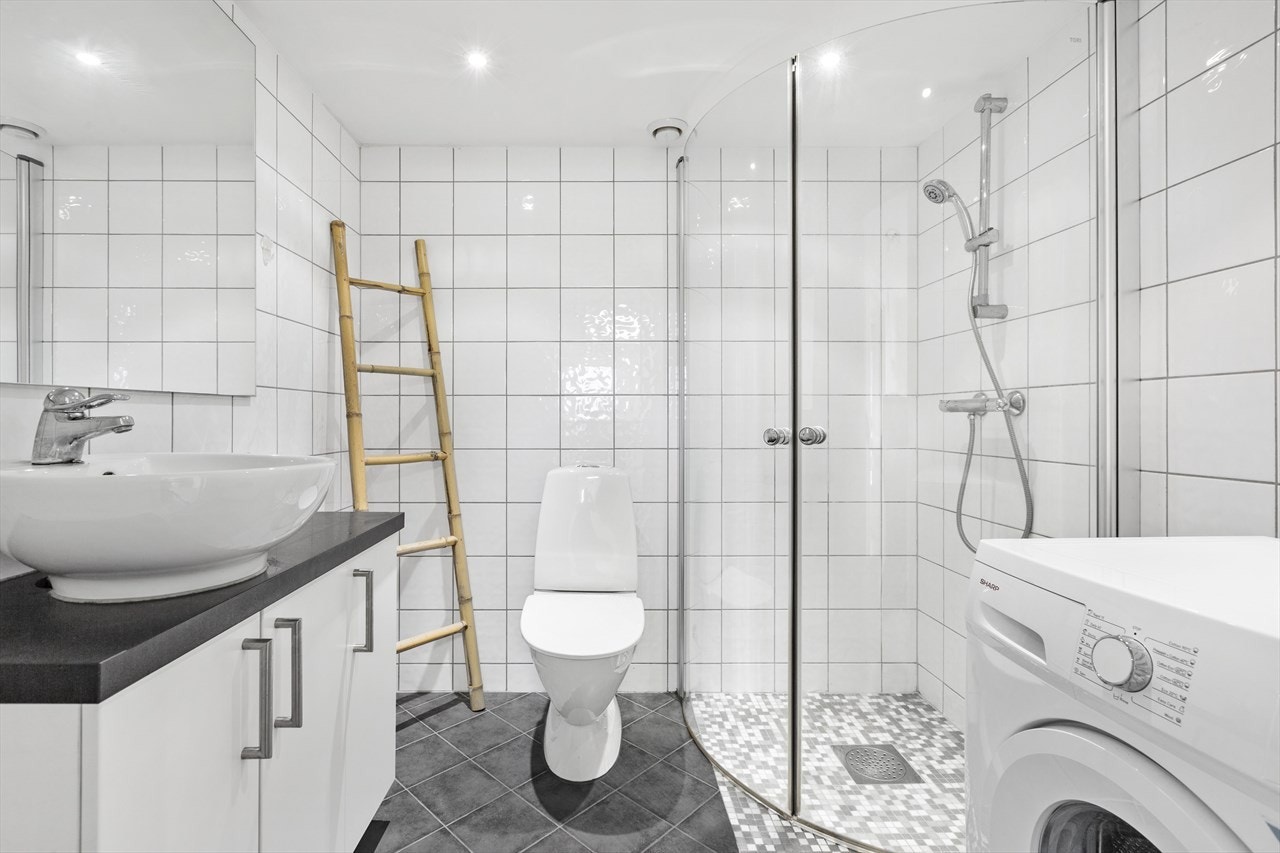 Lekkert bad med flislagte vegger og gulv, downlights i himling og opplegg for vaskemaskin Galleribilde