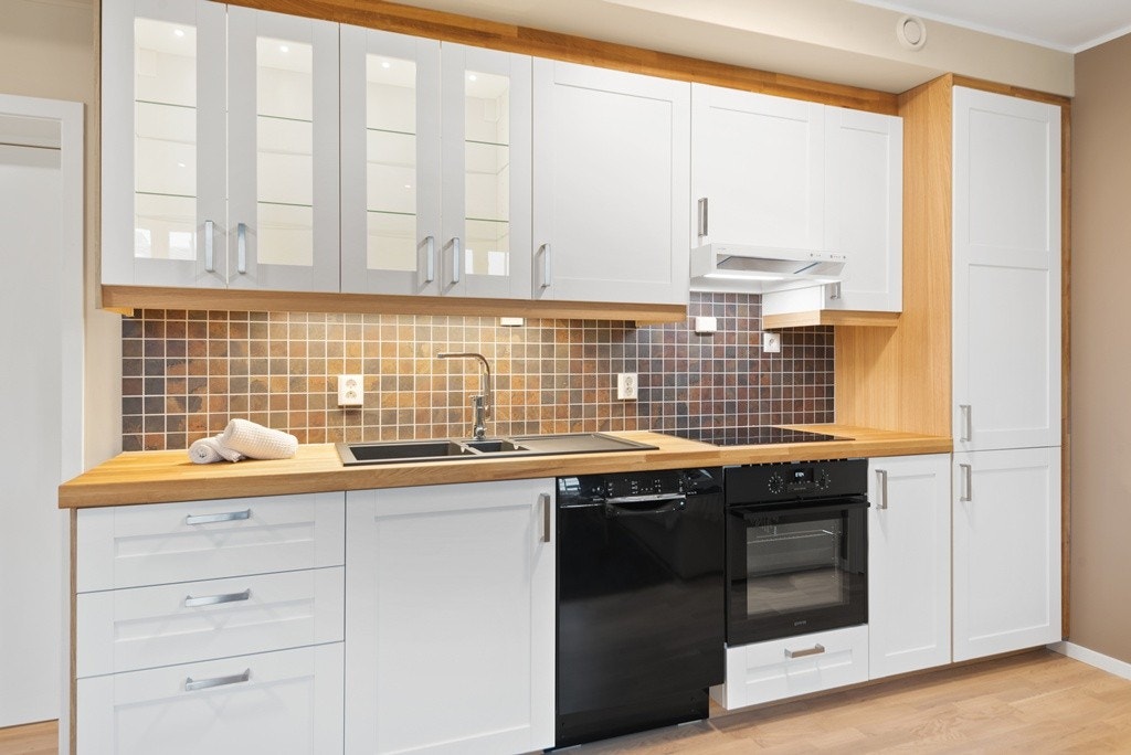 Åpen kjøkkenløsning med moderne standard; integrerte hvitevarer, flis over benken og belysning i skapene. Eksempelbilde. Galleribilde