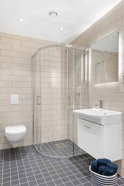 Delikat, flislagt bad med dusjvegger i glass, behagelig gulvvarme og vegghengt wc. Downlights i tak. Bilde fra visningsleilighet, kan avvike. Galleribilde