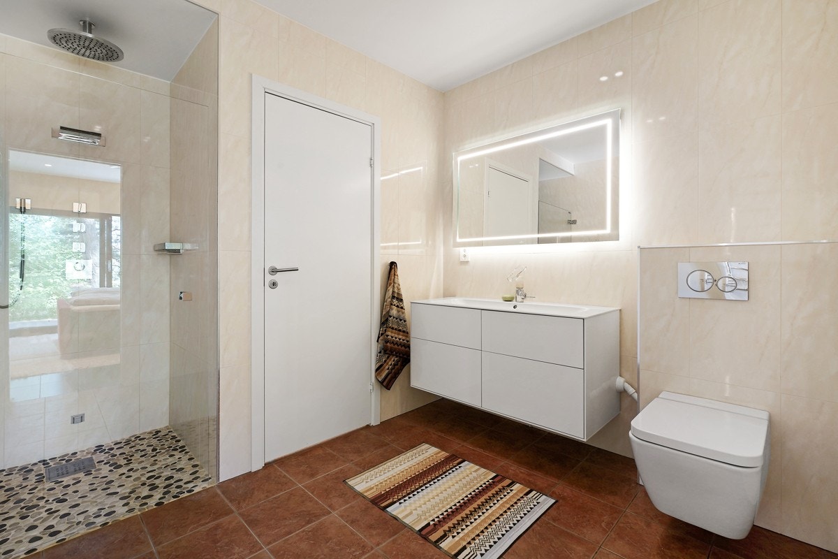 Badet har jaspisrøde fliser på gulv med gulvvarme, marmorerte veggfliser og glatt himling med downlights. Galleribilde