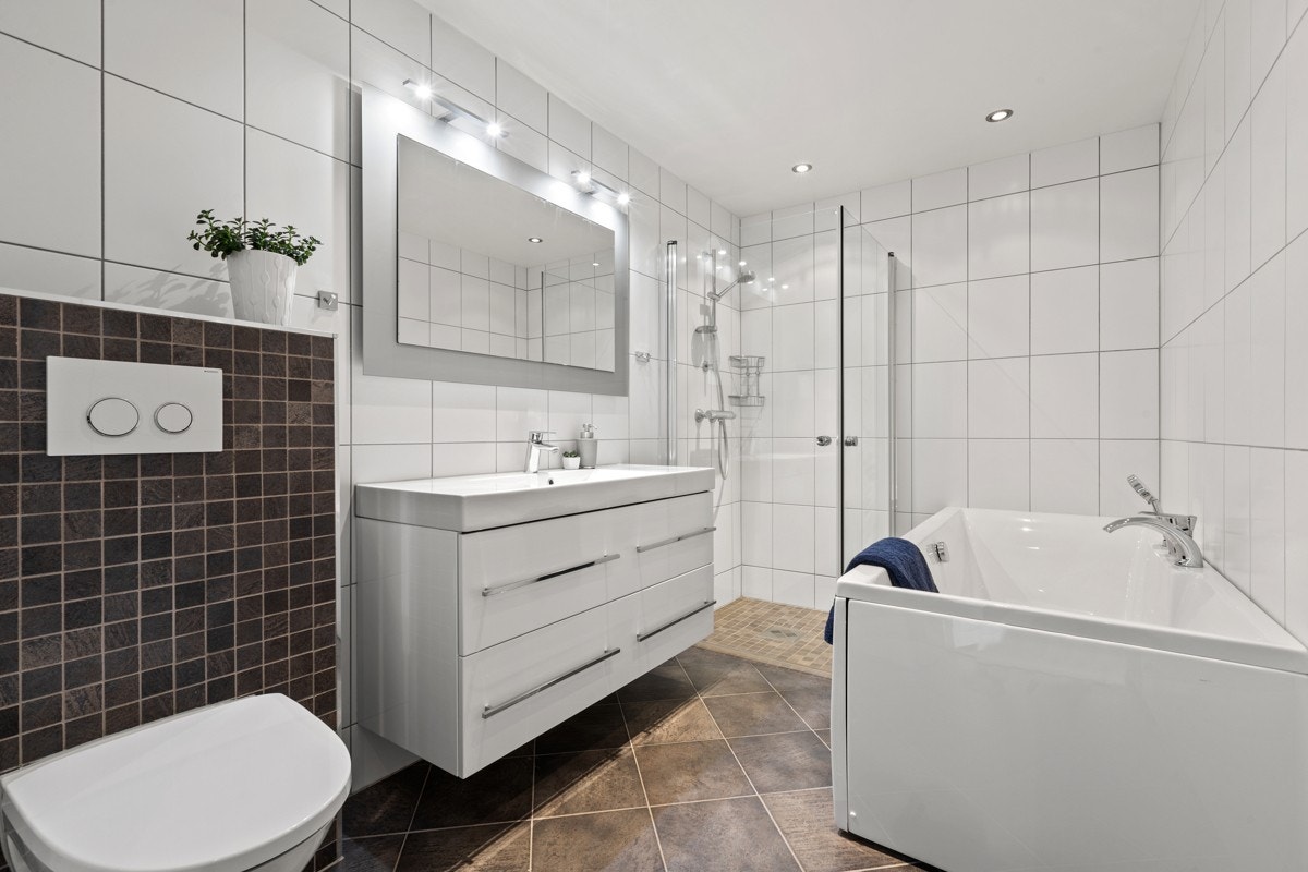 Stort og flott bad med både dusj i nisje, badekar, skuffeseksjon med heldekkende servant og vegghengt wc Galleribilde