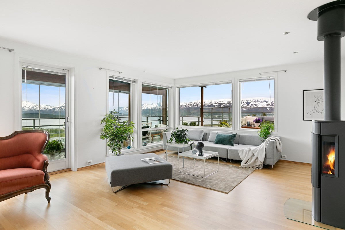 Romslig stue med store glassflater, belysning via downlights og vedfyring