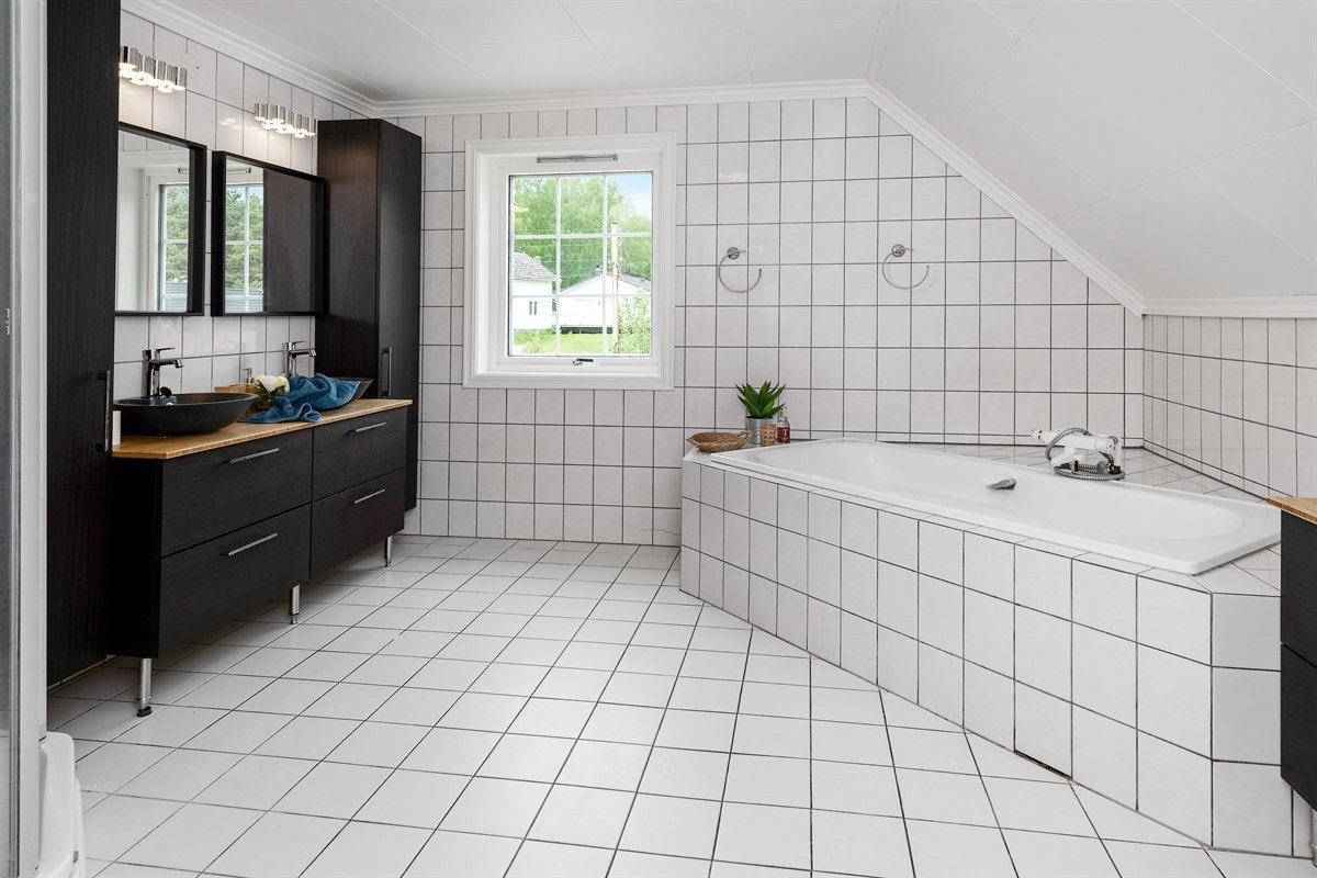 Badet i andre etasje har lyse fliser på gulv og vegger, gulvvarme og en meget familievennlig innredning. Innredningen er fra 2019 og har sorte fronter, flere skuffer, to høyskap, en frittstående kommode og to bolleservanter på trehvit benkeplate. Galleribilde