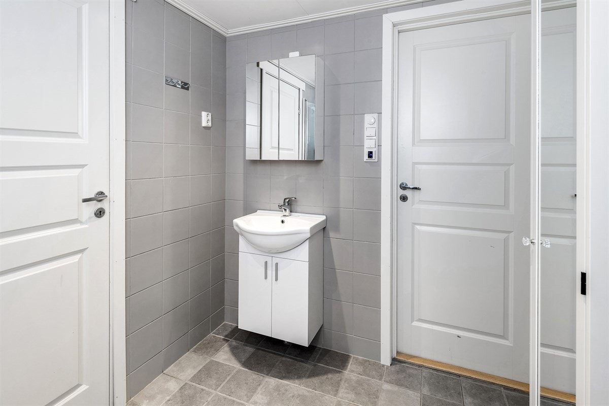 Badet har veggmontert toalett, hvitt servantskap med heldekkende servant og et speilskap. Galleribilde