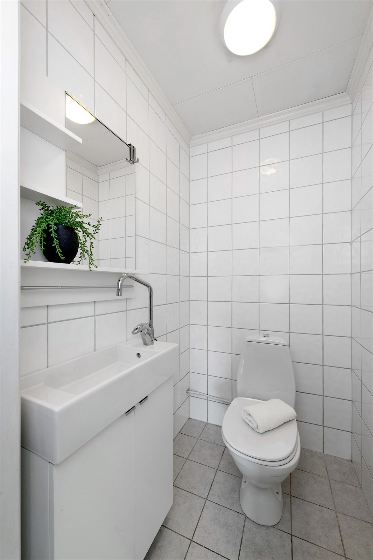 Toalettrommet har fliser på gulv og vegger, og varme i gulv. Det er innredet med toalett, servant på hvitt skap og hylle med speil. Galleribilde