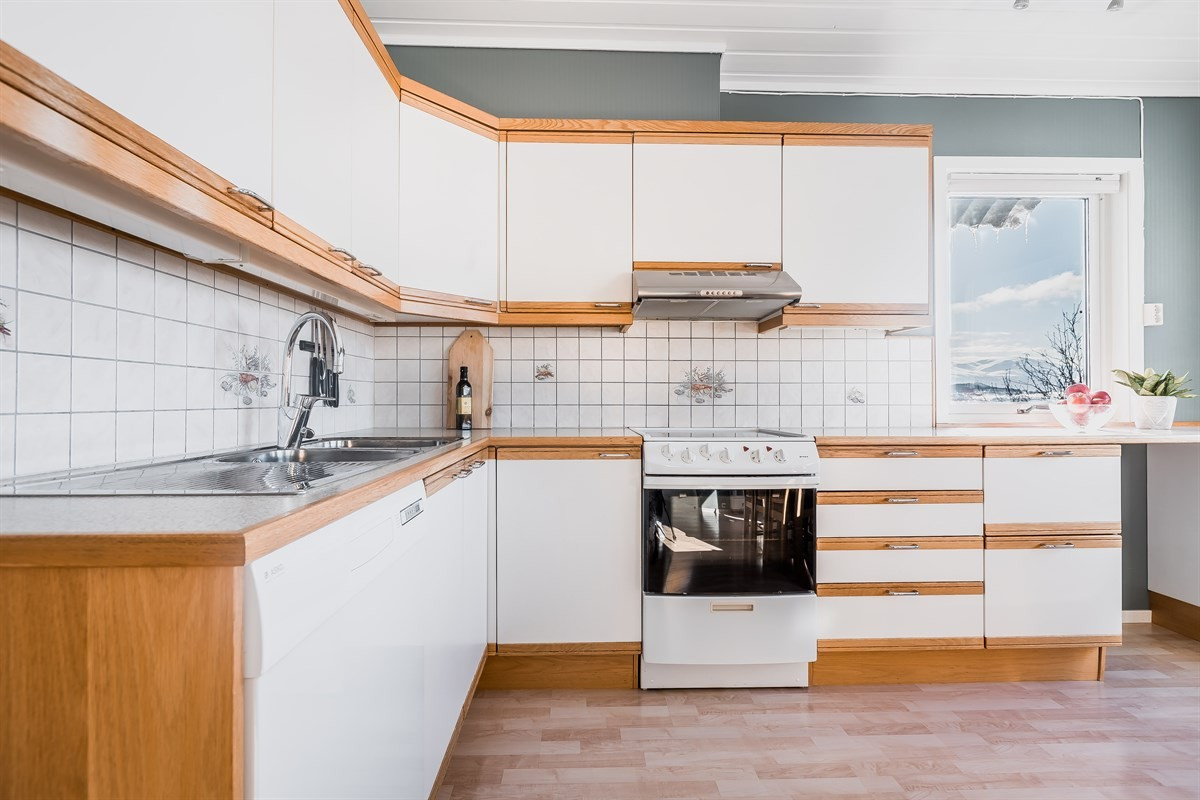 Kjøkken med lyse fronter av laminat. Benkeplate av laminat med nedfelt dobbel oppvaskkum og avrenning. Flis på vegg over benkeplate.