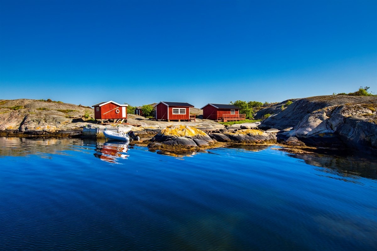 I den lune bukta på holmens nordøstside, hvor morgenbadet kan tas fra de glattskurte svabergene, den brennende sola kan nytes på bryggekanten og lukten av salt kan kjennes fra soverommene, ligger hyttene - vakkert plassert i sjøkanten. Galleribilde