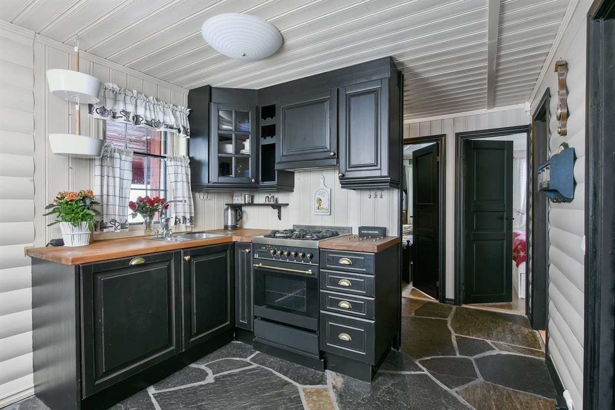 Kjøkkenet er stilfullt og trivelig innredet, med mørke, profilerte fronter, vitrineskap og en heltre benkeplate med nedfelt oppvaskkum. Galleribilde