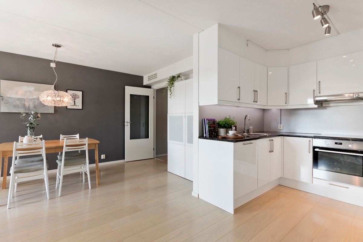 Kjøkkeninnredningen er hvit med høyglanspolerte fronter, laminat benkeplate og lys under overskap. Galleribilde