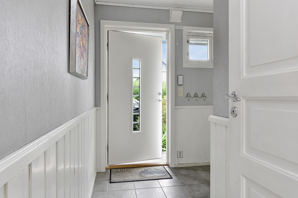 Rekkehuset har en praktisk, vinklet entré, med lysegrå gulvfliser, tapetsert, lysegrå veggflater, hvitt brystningspanel, og gulvvarme. Galleribilde