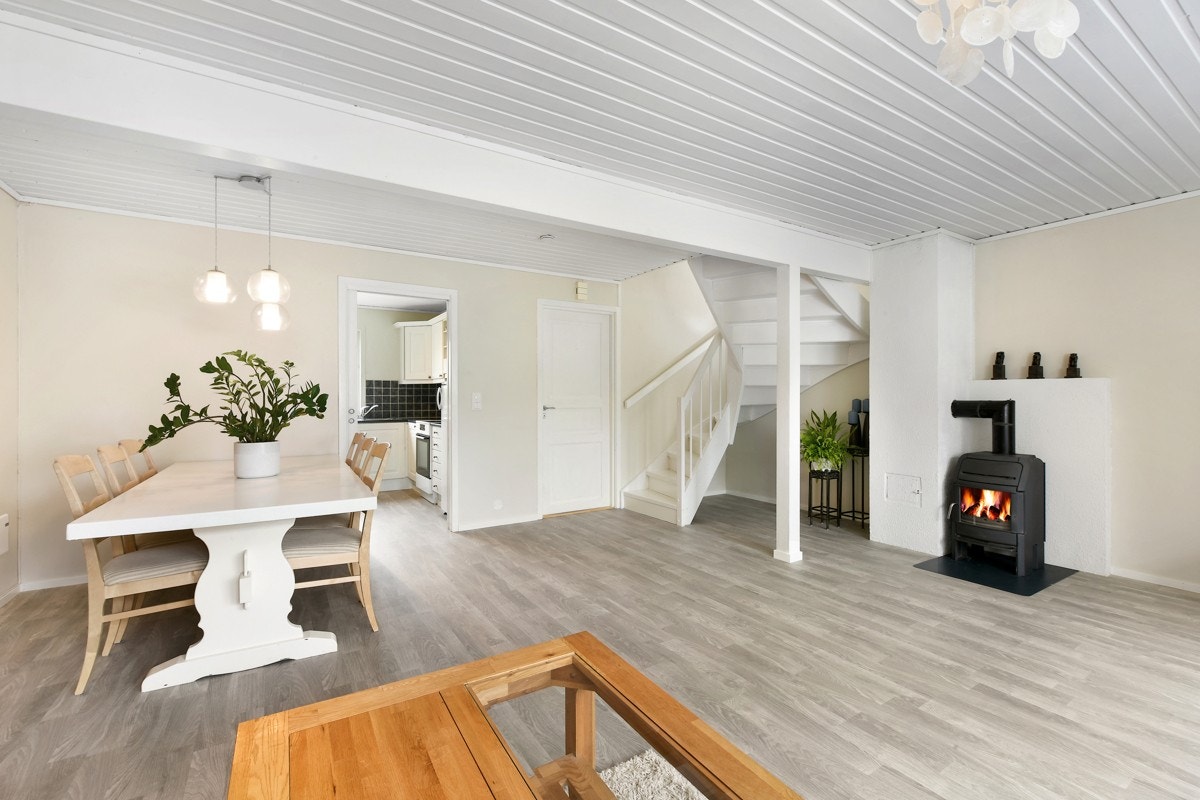 Til hvitmalt pipeløp er det koblet en kledelig peisovn. Fra stuen leder en hvitmalt tretrapp opp til andre etasje. Galleribilde