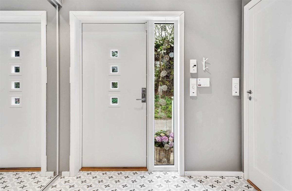Boligen har adkomst via overbygd inngangsparti og en hvit ytterdør med glassfelt som slipper lyset inn i entreen. Galleribilde