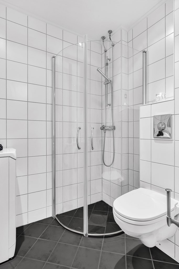 Innredet med dushjørne med innsvingbare glassdører, vegghengt wc og servant med skap. Galleribilde