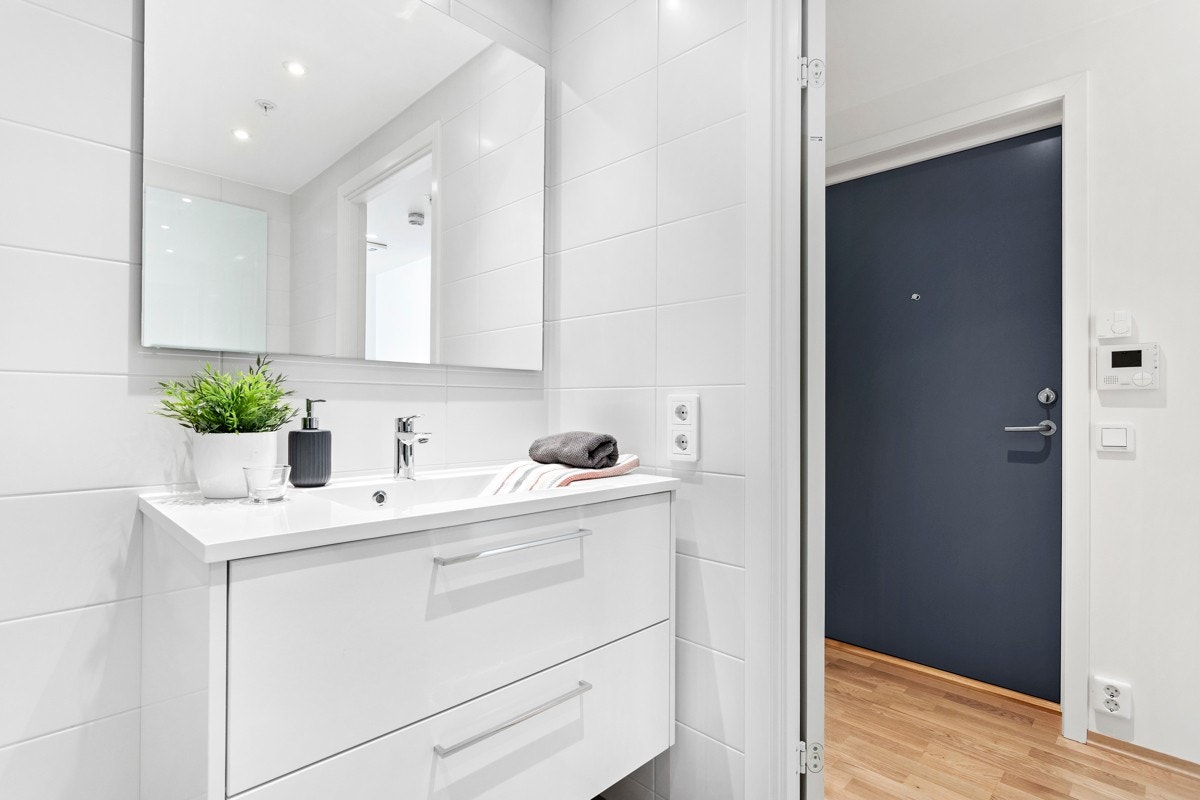 Baderomsinnredningen er stilren med hvit servant og hvit innredning med underskuffer, speil med belysning over innredning, ettgreps servantbatteri, veggmontert toalett med dempet toalettsete, rette dusjvegger i glass m.m. Galleribilde