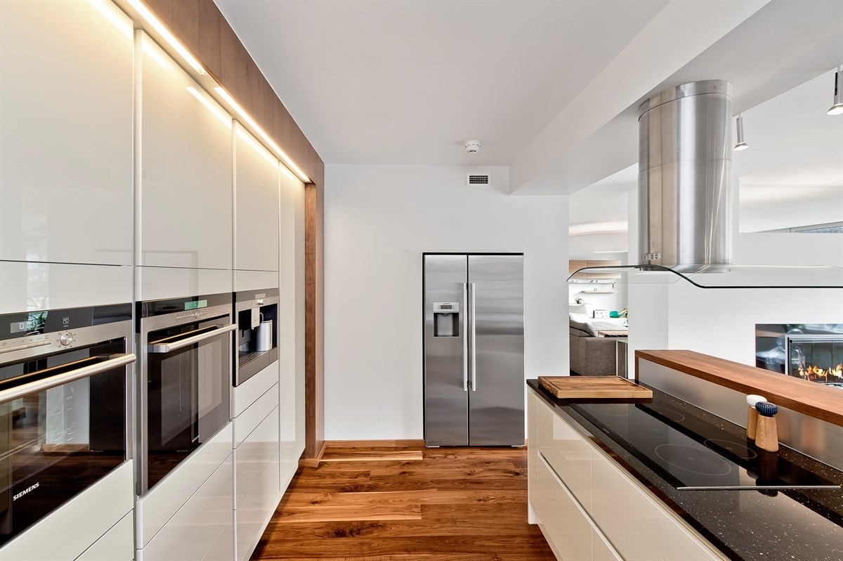 Kjøkkeninnredningen har hvite høyglansfronter, samt en eksklusiv marmorbenkeplate. Galleribilde