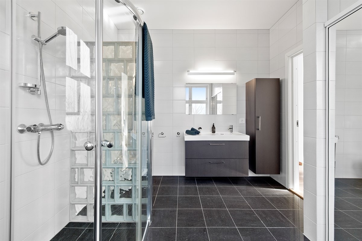 Begge badene i andre etasje har mørke fliser på gulv med varmekabler og lyse fliser på veggene. Galleribilde