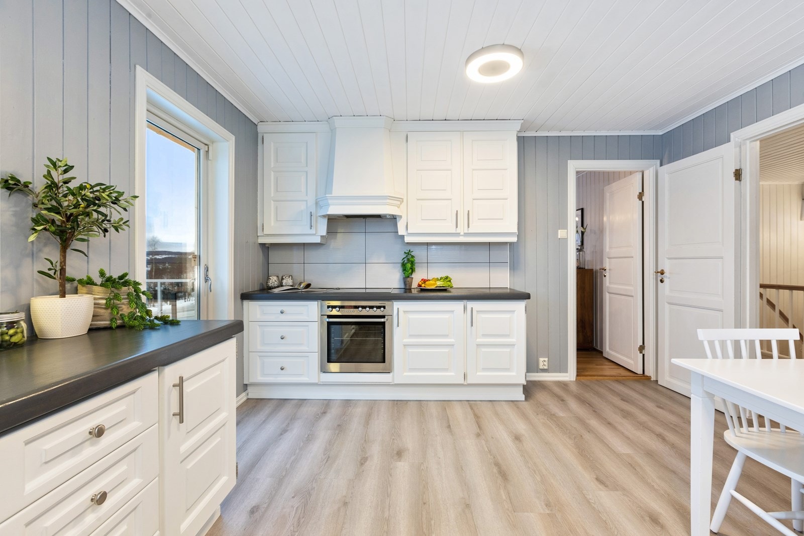 Kjøkkenet har hvite, forseggjorte profilfonter, samt gråmalte benkeplater i heltre. Galleribilde