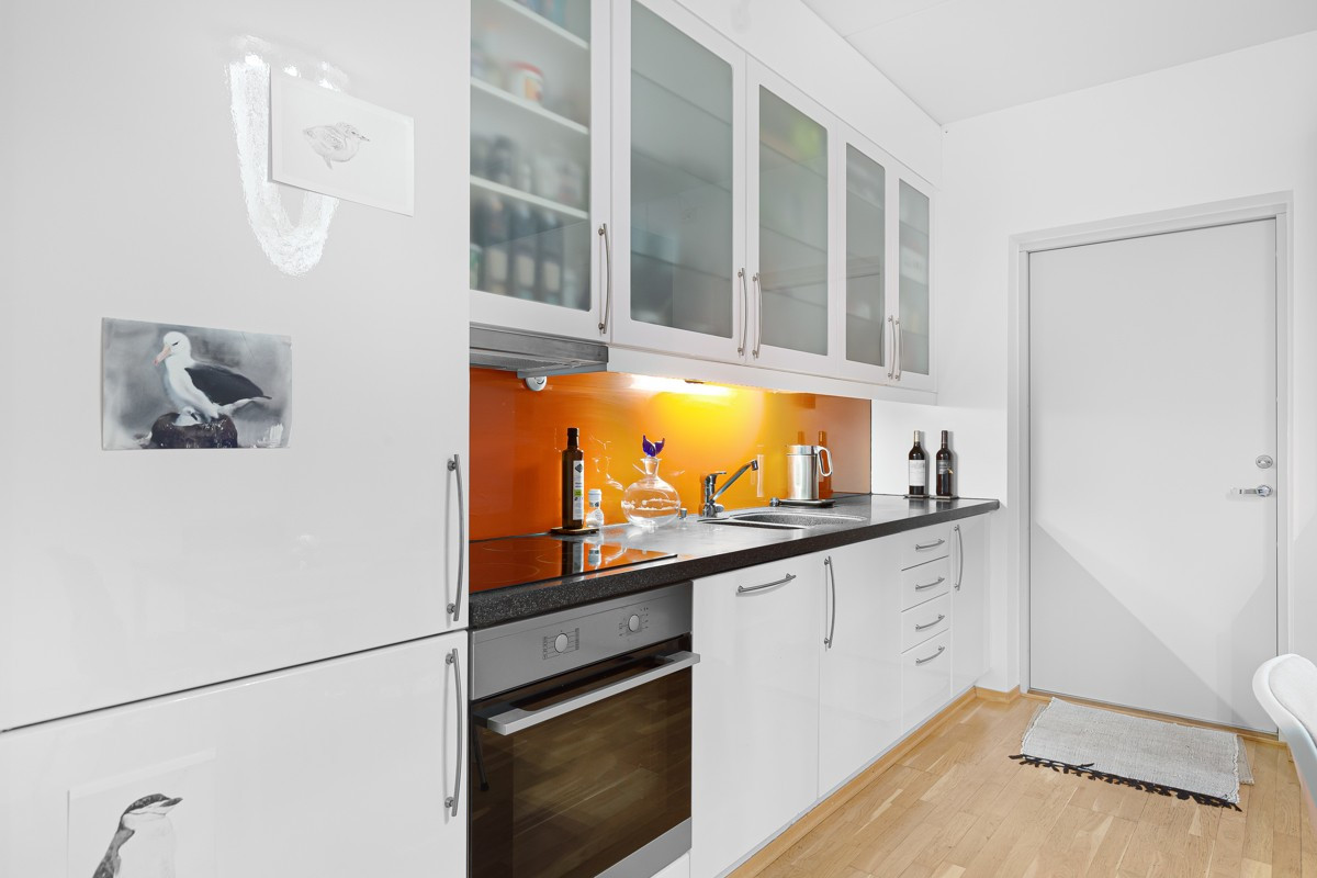 Kjøkken med glatte hvite fronter. Lekker glassplate over benk og integrerte hvitevarer