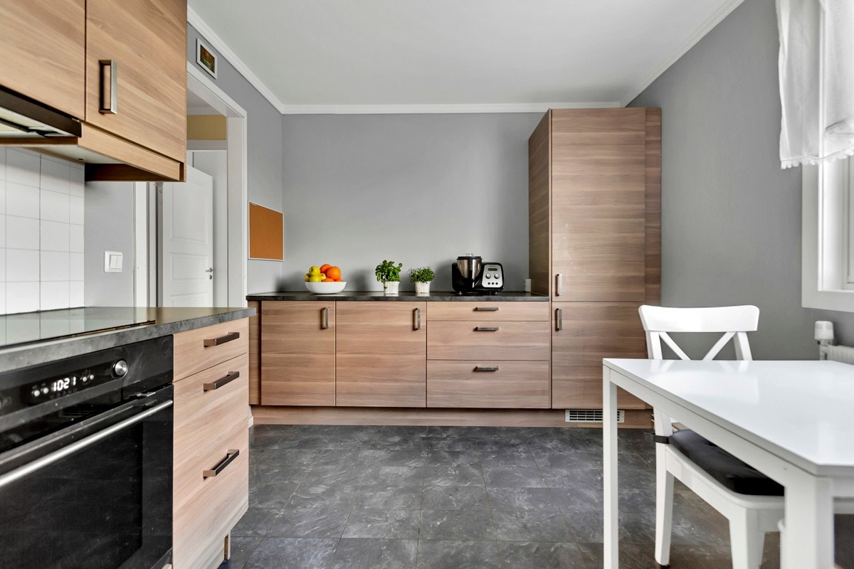 . Innredningen har glatte, finerte fronter, vitrineskap, benkebelysning, lys kitchenboard og laminert benkeplate med nedfelt kum i stål Galleribilde