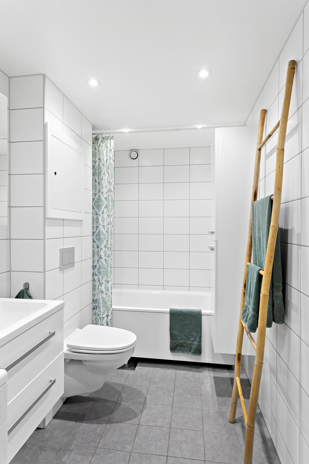 Badet er innredet med vegghengt toalett, servant med underskap, badekar med dusjgarnityr og håndholdt dusj Galleribilde