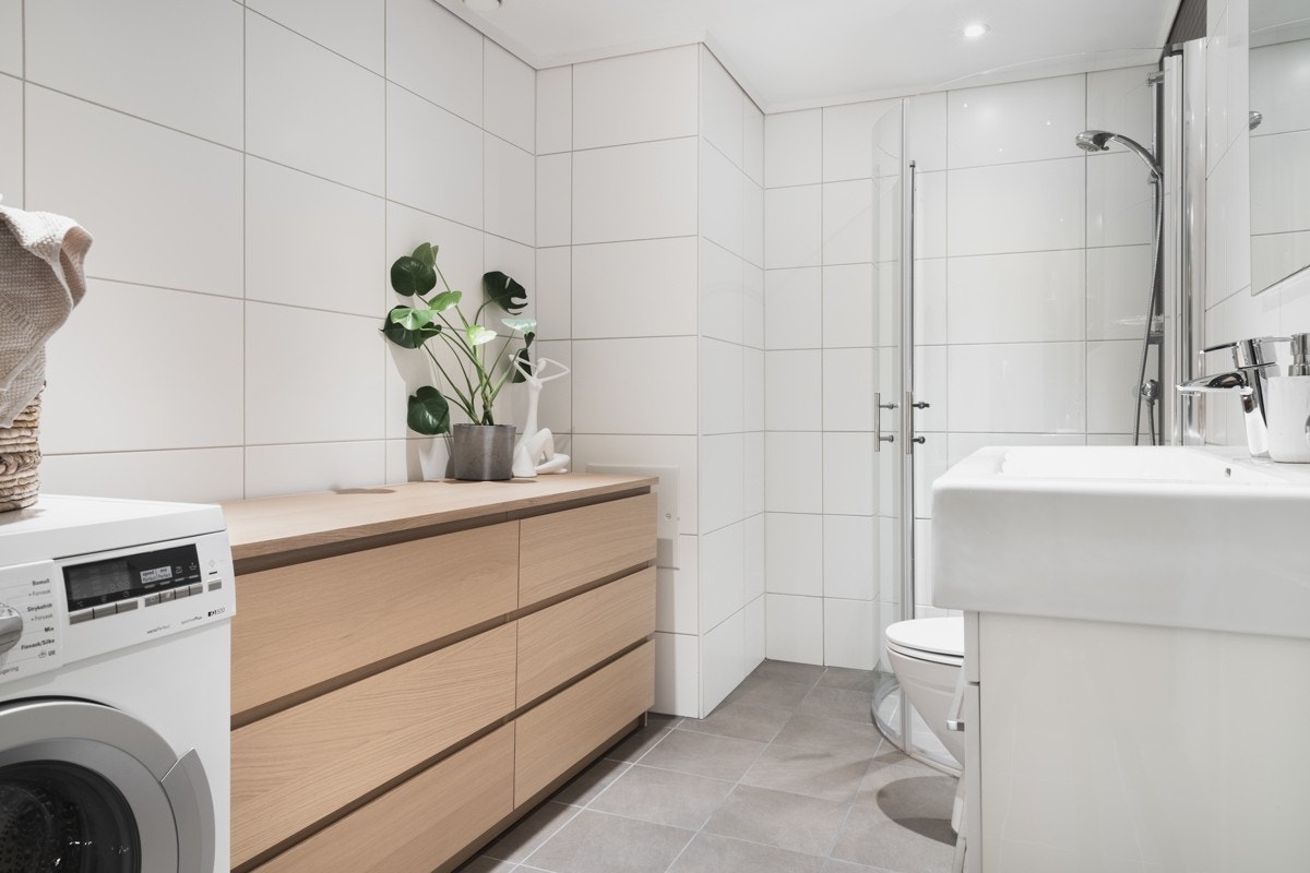 Badet ineholder toalett, servant med møblement, dusjhjørne med glassdører og opplegg for vaskemaskin. Galleribilde