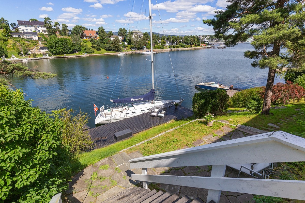 Fra porten i gjerdet går det trapp ned til nok en steinsatt uteplass, og fra denne går det trapper i terrenget ned til brygge og båtplass. Galleribilde