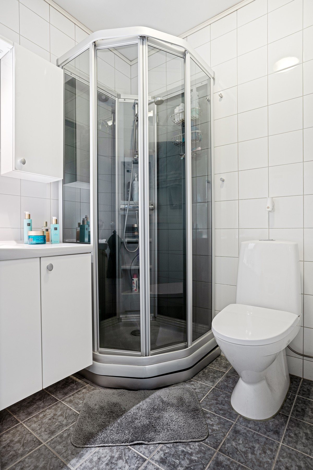 Badet er utstyrt med gulvmontert toalett, dusjkabinett, servant m/innredning og opplegg for vaskemaskin og tørketrommel