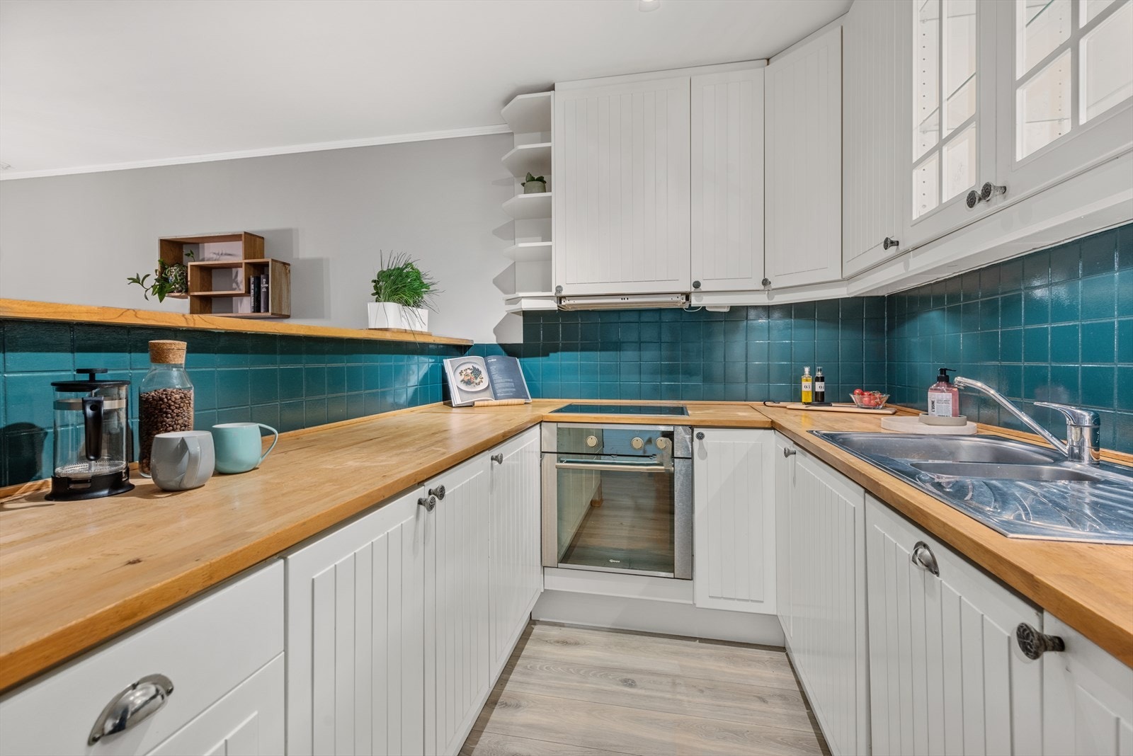 Pent og åpen kjøkkenløsning med kjøkkeninnredning med hvite profilerte fronter og vitrine overskap med innvendig belysning. Galleribilde