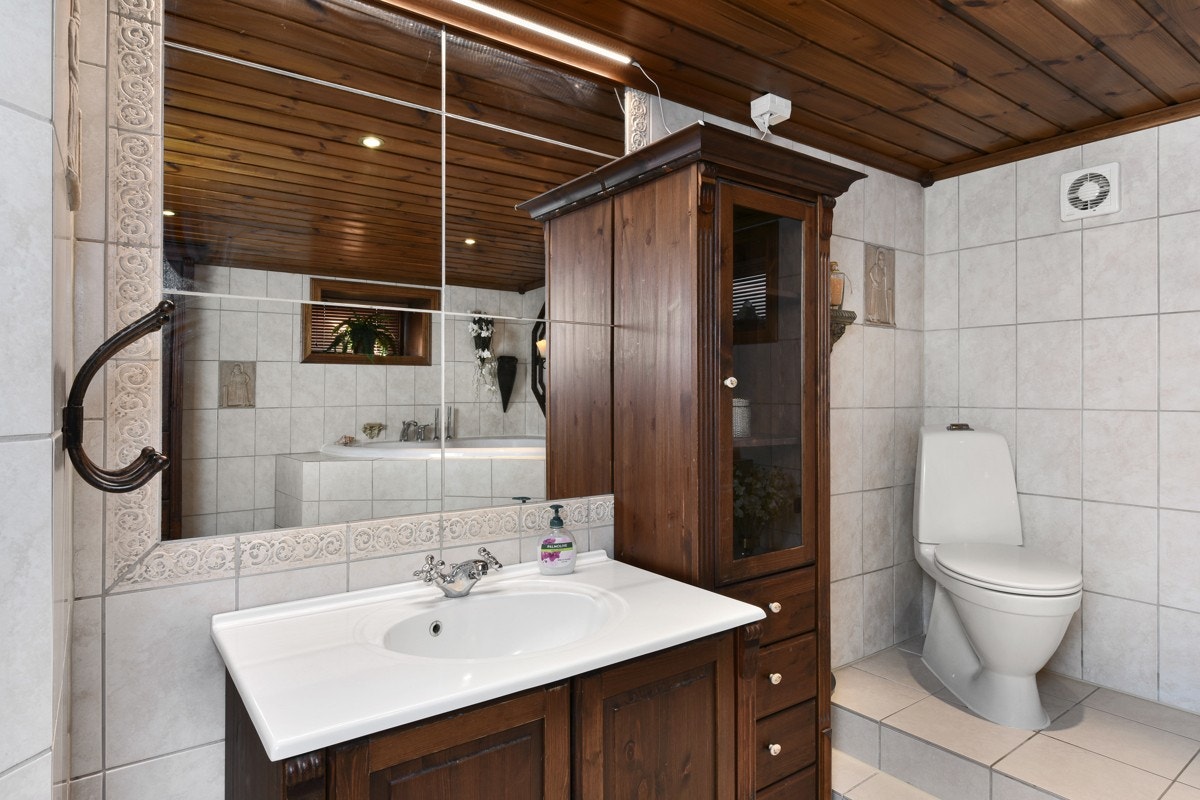 I rommet er det downlights, lysegrå fliser på gulv og trapp opp til badekar, og på vegg er det lyse fliser. Galleribilde