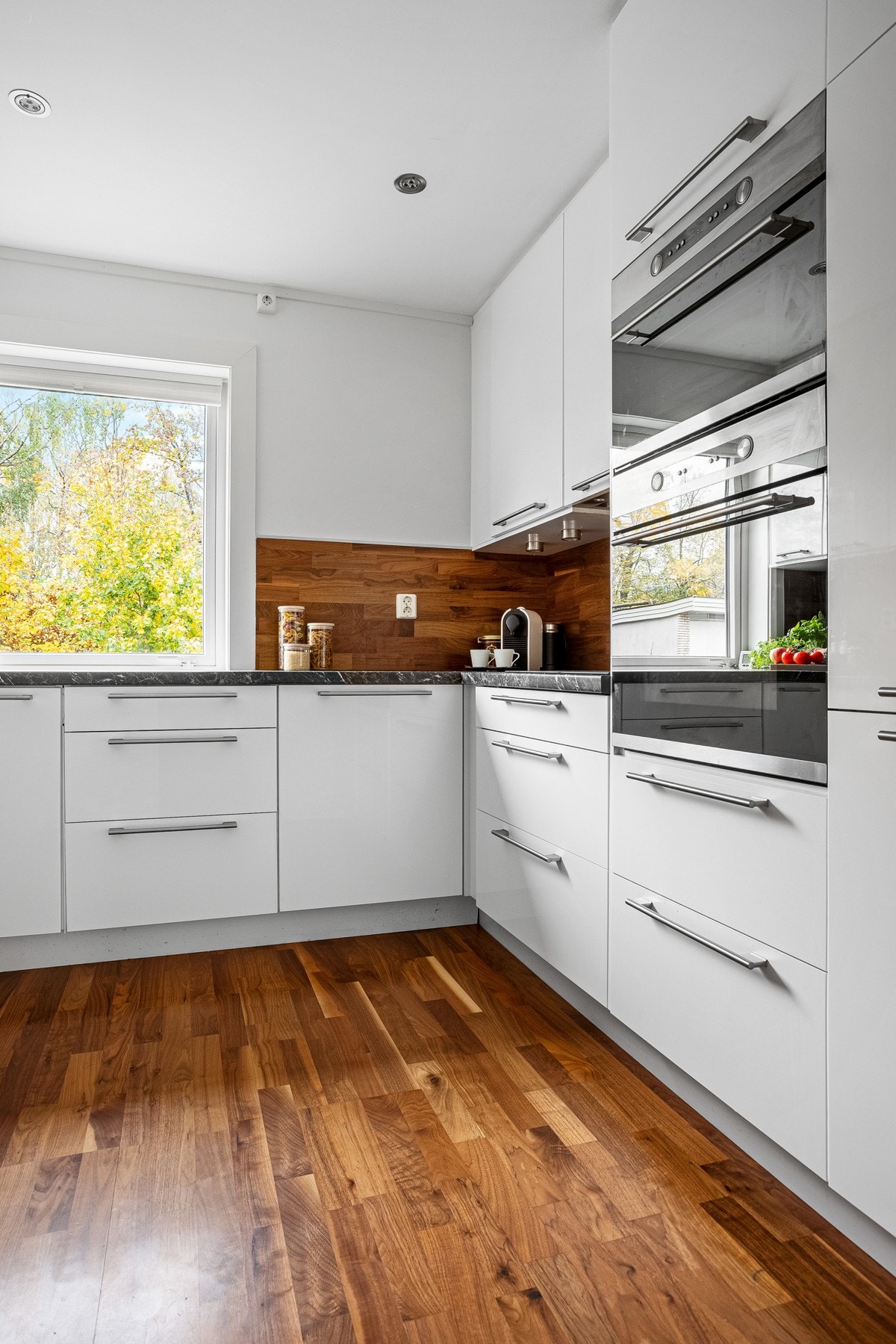 Innredet med glatte høyglansfronter, laminat benkeplate, ventilator, oppvaskkum, parkett på vegg over benk og integrerte hvitevarer. Galleribilde