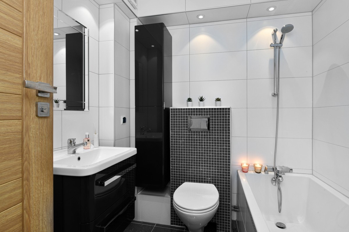 Badet har grå gulvfliser, hvite veggfliser, og grå mosaikkfliser på sisternekasse. Galleribilde