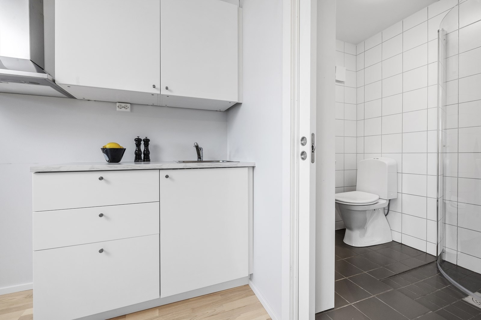 Bad og wc har klassiske hvite fliser på vegg og tidsriktige grå gulvfliser Galleribilde