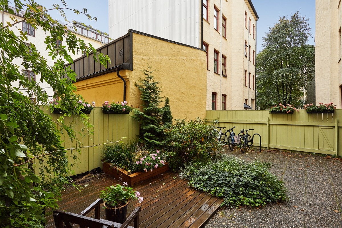 Felles bakgård belagt med betongheller, platting med sittegruppe, prydbusker og diverse beplantning. Galleribilde