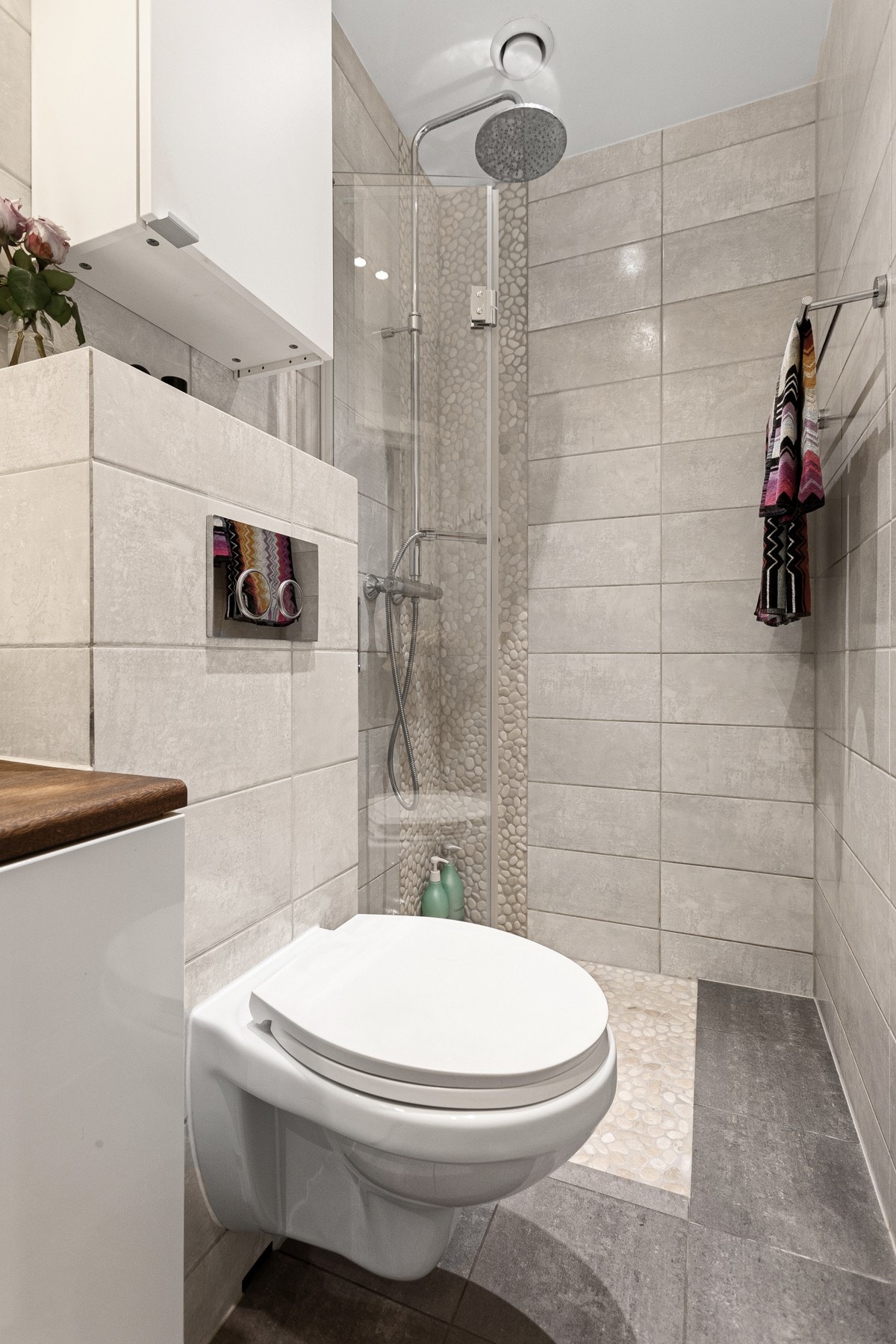 Dusjsonen har fine elvesten på gulv og vegger, innfellbar glassdør og både hånd- og regnfallsdusj. Baderommet er også utstyrt med vegghengt toalett og ekstra vegghengt skap. Galleribilde