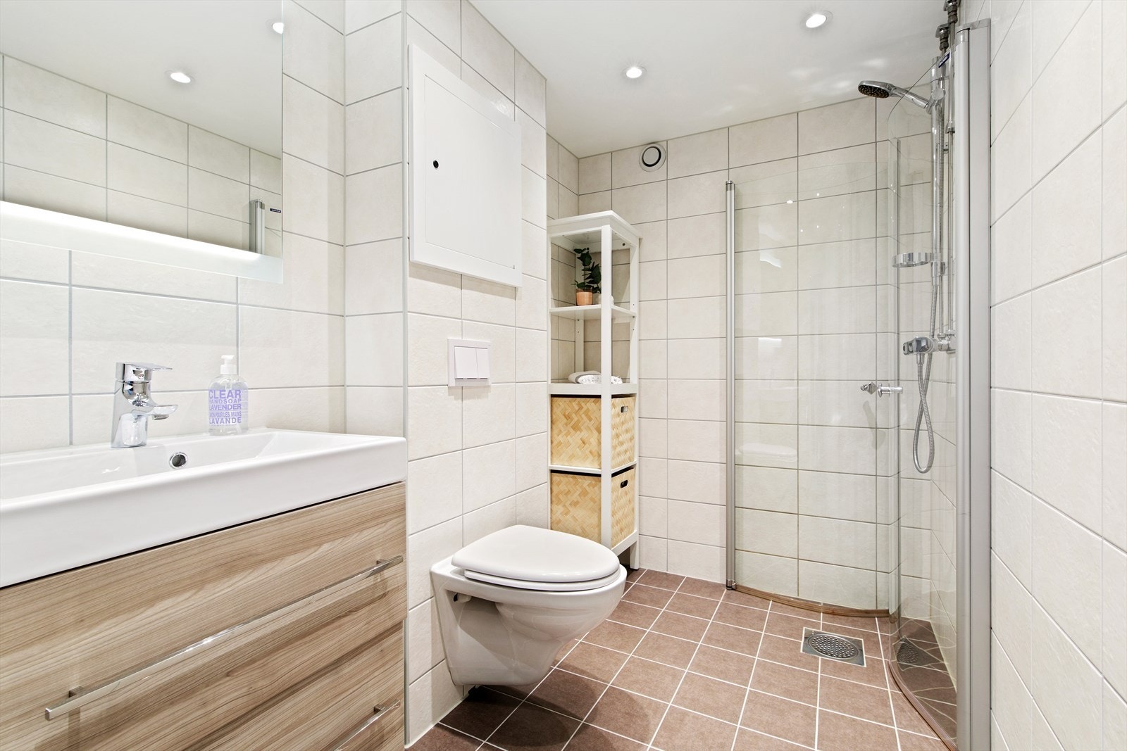 Her er det downlights i tak, dusjhjørne, vegghengt toalett, servant med skuffeseksjon, speil med integrert belysning, samt opplegg for vaskesøyle. Galleribilde