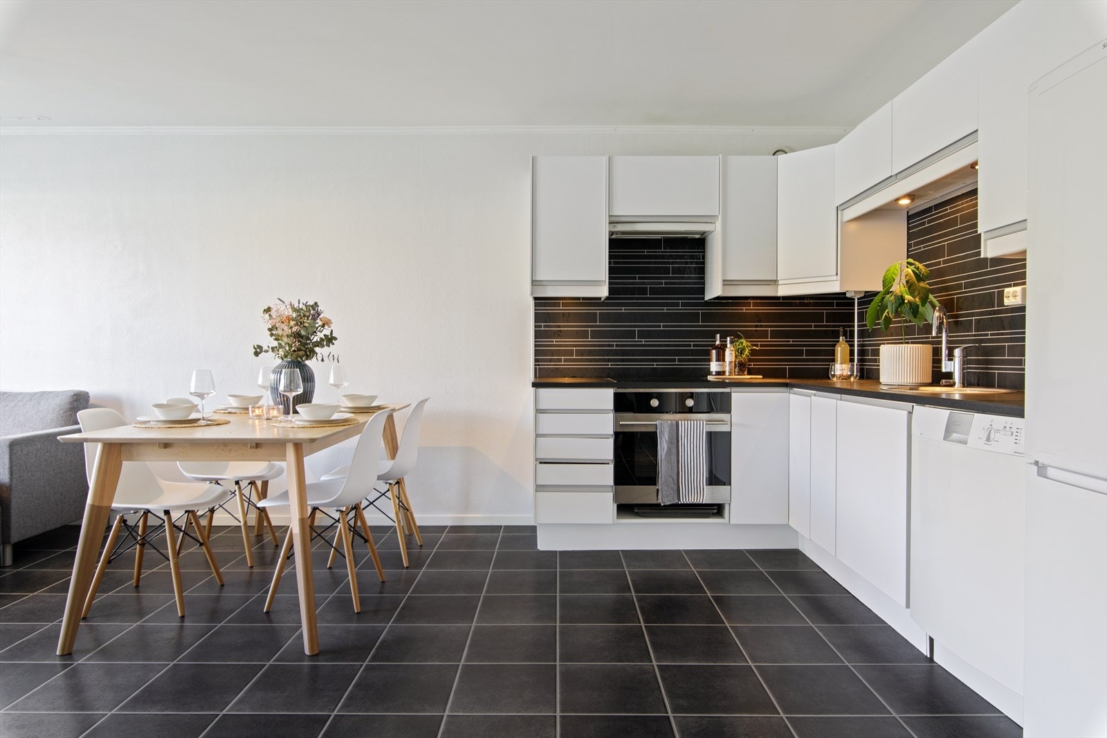 Kjøkkenet er innredet med hvite glatte fronter, laminat benkeplate, samt plater på vegg over benkeplaten. Galleribilde