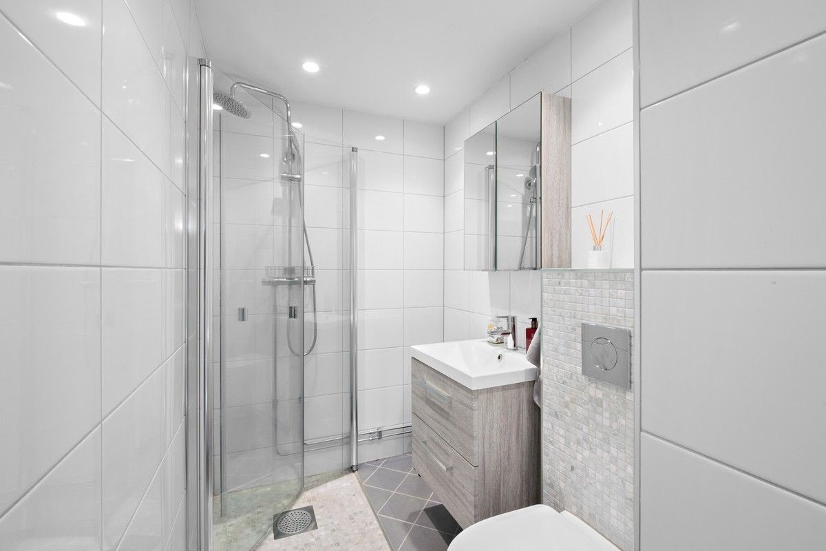 Dusjsone med innfellbare dører, servant med underskap, speilskap, vegghengte hyller samt en arbeidsbenk. Veggfestet wc Galleribilde