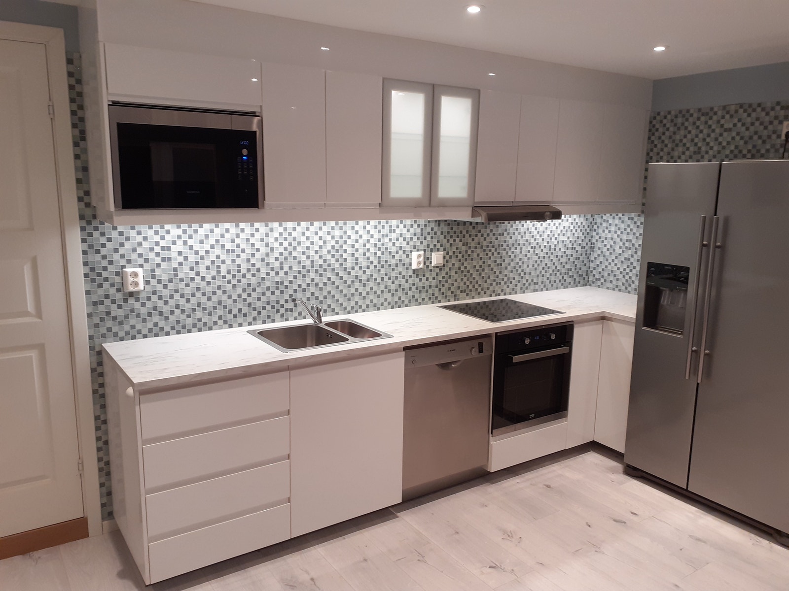 Kjøkken med oppvaskmaskin, mikro, ovn og kjøleskap med frys. Hvit høyglans IKEA kjøkken med lys i glass skap. Nytt kjøkken fra 2020 Galleribilde