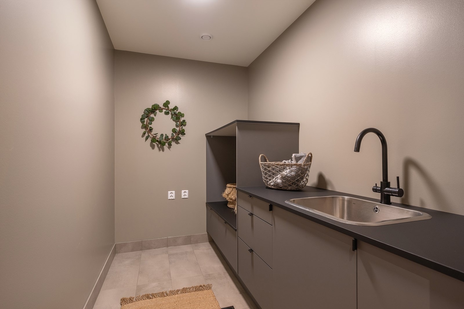 Vaskerommet er praktisk og stilfullt innredet. Rommet har fliser på gulvet med gulvvarme, veggene er malt grå og innredningen har grå, glatte fronter. Galleribilde