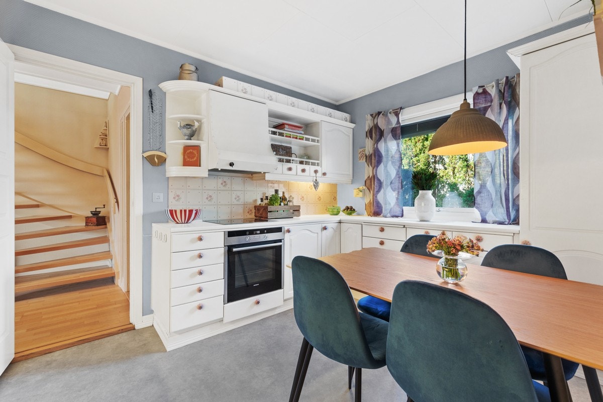 Pent kjøkken med klassisk innredning i form av hvite folierte, over- og underskap og laminat benkeplate Galleribilde